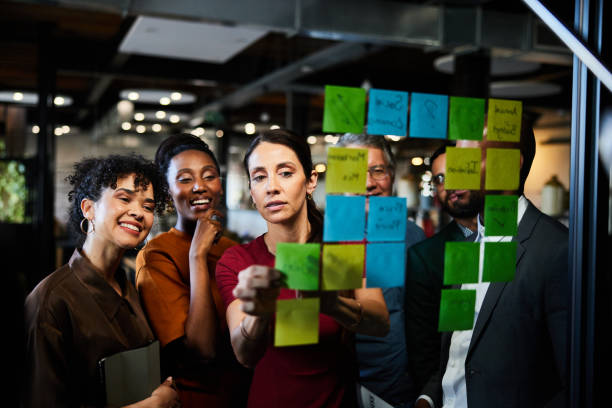 istock Smiling businesspeople brainstorming using adhesive notes on a glass wall in an office 2077806383