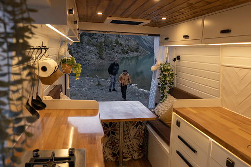 Interior view of a camper van and a father and his son at sunset playing throwing stones into the lake.\nConcept van life, lifestyle, people, transportation, vacations, tourism