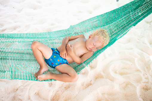 Baby sleeping on tropical beach. Child relaxing in hammock. Infant taking a nap after swimming fun. Vacation with young child. Holiday with toddler.
