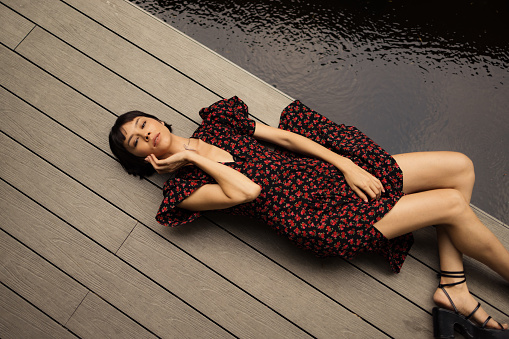 High angle view of beautiful Asian woman lying on wooden pier by the lake and looking at camera.