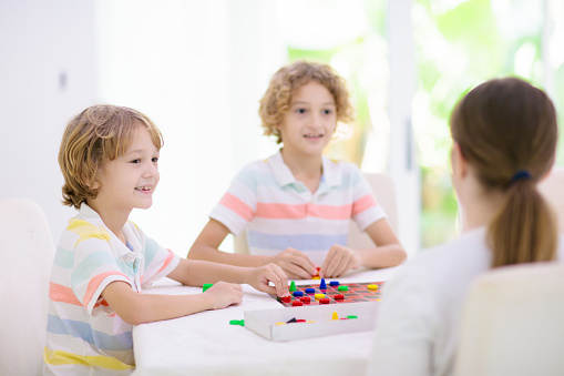 Family playing board game at home. Kids play strategic game. Little boy throwing dice. Fun indoor activity for summer vacation. Siblings bond. Educational toys. Friends enjoy game night.