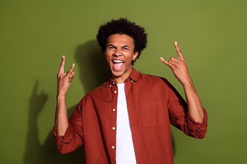 Photo portrait of attractive young man show horns gesture rock roll music wear trendy brown clothes isolated on khaki color background.