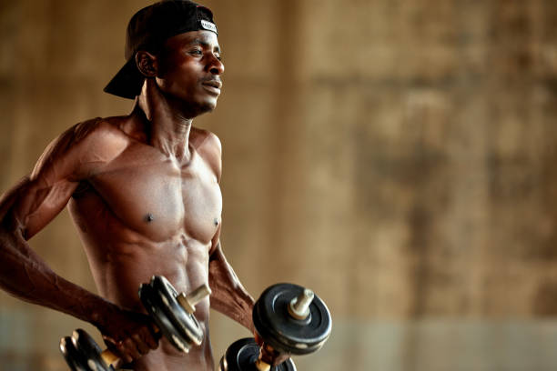 attractive african american man smiling and doing exercise with dumbbells. - shirtless men jock american culture 뉴스 사진 이미지