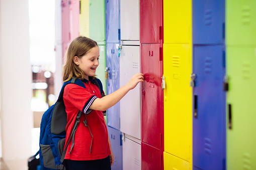 Student in school at locker. Kids study. Little girl in uniform holding padlock key in preschool hall. Child with backpack and books.