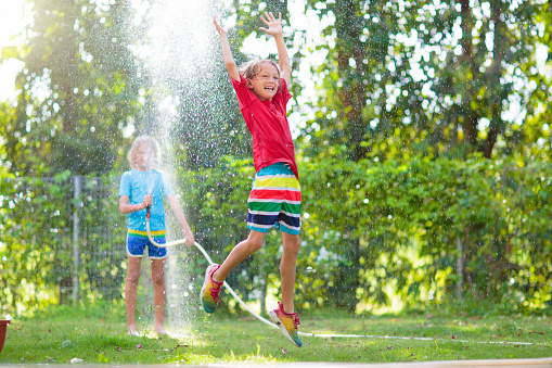 Kids play with water sprinkle hose. Summer garden outdoor fun for children. Boy splashing water on hot sunny day. Kid watering plants in backyard. Toy water gun.