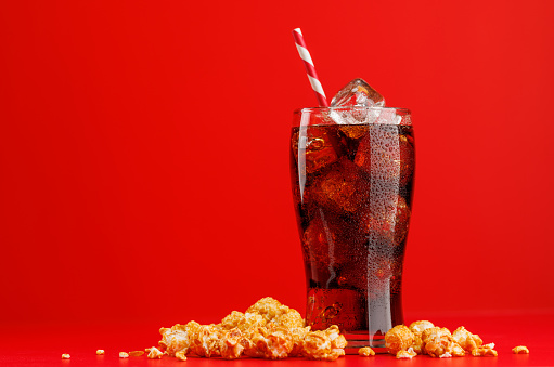 Cola with ice and popcorn over red background, with copy space