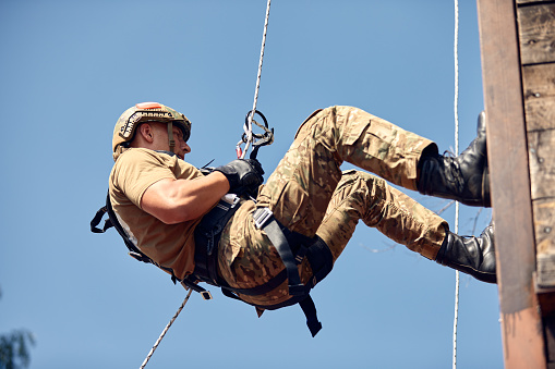 Military soldier climbing net during obstacle course in boot camp.