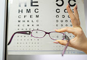 A woman holding eyeglasses in front of an eye chart