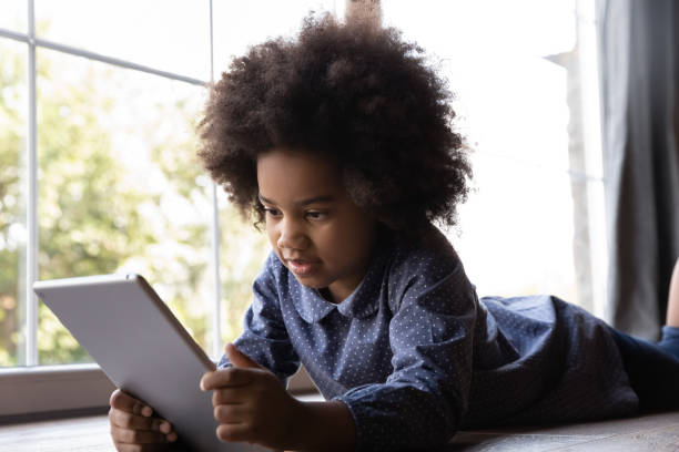 istock Cute African girl lying on floor indoor with digital tablet 2078036457