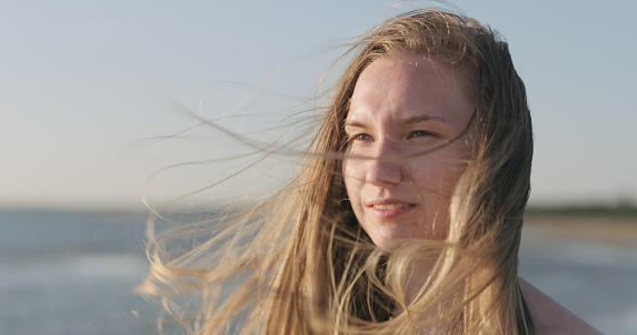 closeup portrait of young girl standing on a beach and wind blows her hair, wide photo