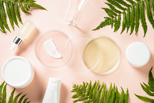 Cosmetic laboratory concept . Glass petri dish with cosmetic products and green plants. Flat lay image.
