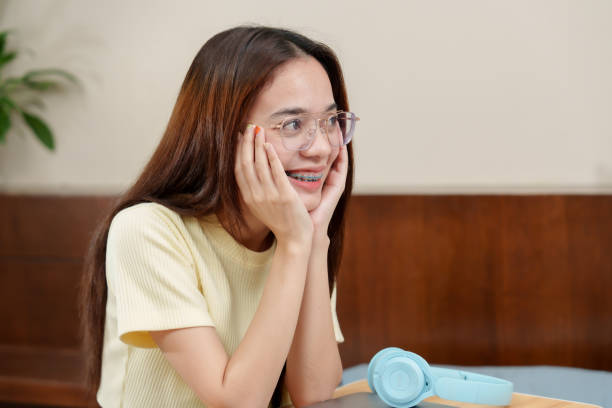 istock Asian adult chuckling, light vision aids perched, fingers frame face, cozy home interior with a tranquil aura. glasses aloft, dental braces in sight, hands caressing cheeks, homely room ambiance. 2078141815