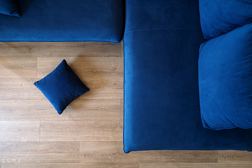 High above view of blue comfortable elegant couch and pillow on wooden floor in modern living room at apartment. Cozy space for rest at home. Flat lay.