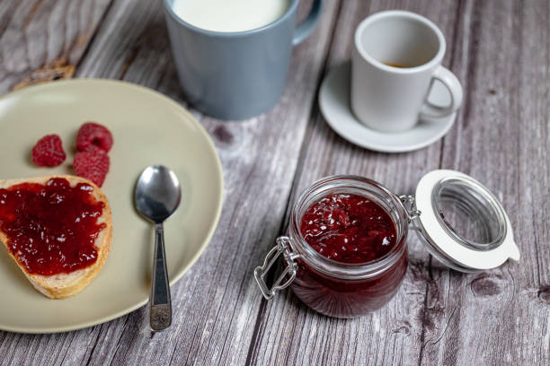 Homemade raspberry jam in glass jar, healthy breakfast with toast, raspberry jam, milk in cup and Italian espresso coffee, top view