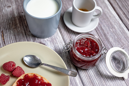 Homemade raspberry jam in glass jar, healthy breakfast with toast, raspberry jam, milk in cup and Italian espresso coffee, top view