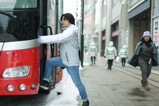 Man traveling in winter is about to board a tour bus on the street in Hokkaido, Japan