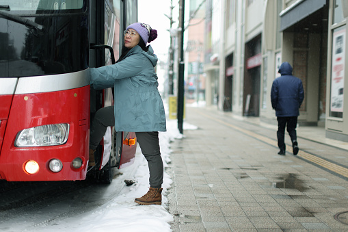 Woman traveling in winter is about to board a tour bus on the street in Hokkaido, Japan