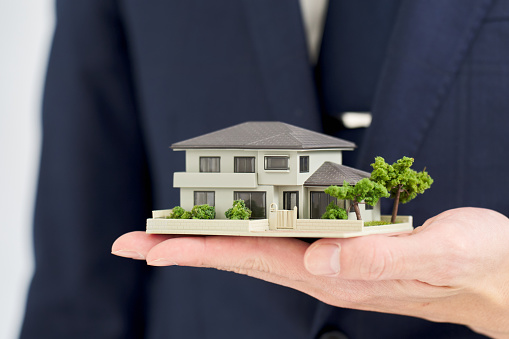 Hand of a businessman holding a model of a house