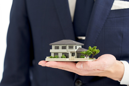 Hand of a businessman holding a model of a house