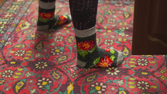 legs in colorful ornate warm wool socks on old ornate red carpet