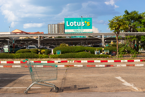 Pattaya, Thailand - 18 December, 2023: Empty shopping cart in a Lotus's supermarket parking lot. Giant billboard of Lotus's Shopping Mall. Formerly Tesco Lotus retail chain