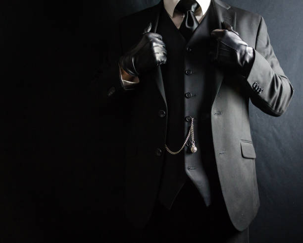 Portrait of retro young african american man wearing black suit and fedora hat staring at camera. Young male model posing against gray background. Vertical studio photography from a DSLR camera. Sharp focus on eyes.