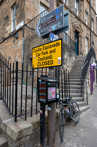 Edingburgh, Scotland, UK – June 17th, 2023: Directional signs, as well as a vending machine for city maps. A bicycle is attached to the gate of a house where a staircase leads to the entrance