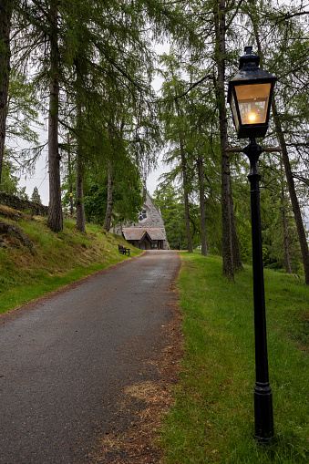Crathie, Scotland, UK – June 19th, 2023:  Driveway with burning lantern. View on Crathie Kirk, the presbyterian church near Balmoral castle in Scotland