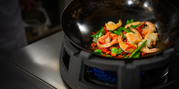 Stir-frying vegetables with prawns in a wok in a professional kitchen.
