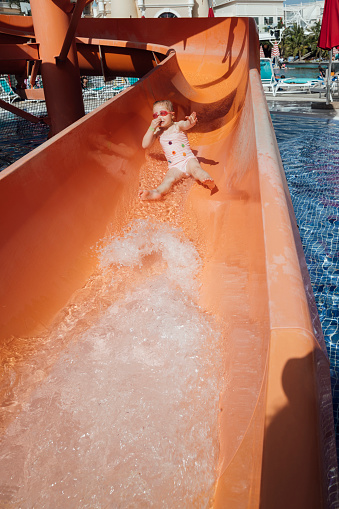 A young girl wearing a swimsuit and goggles on holiday, playing at a waterpark at an all inclusive hotel in Tenerife, Spain. She is sliding down a waterslide as she holds her nose.