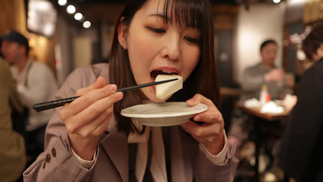 Young business woman eating Oden Japanese food in Izakaya bar after work - part 1 of 2
