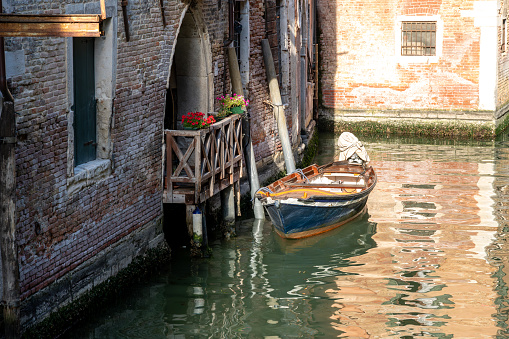 Venice, Veneto - Italy - 06-10-2021: Small boat tied up next to a charming balcony with flowers in Venice