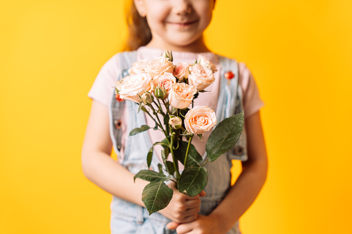 Little girl holding spray roses in her hands against yellow background.