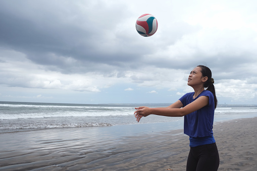 Close-up shot of Indonesian young woman practicing volleyball at the beach during bad weather