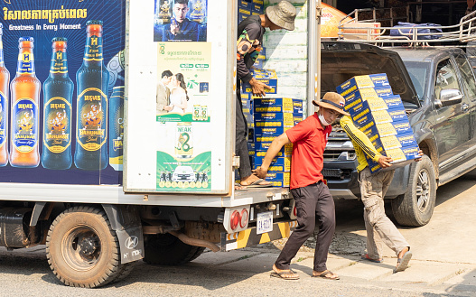 Pramaoy, Pursat, Cambodia on Feb 16, 2024: people carrying a heavy bundles of beer cans into the local street shop; many types of work in Cambodia are still carried out by manual labour instead of being supported by machinery devices