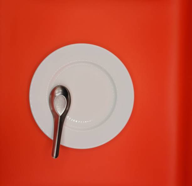 Empty white plate with spoon on red background. Meal preparation concept.