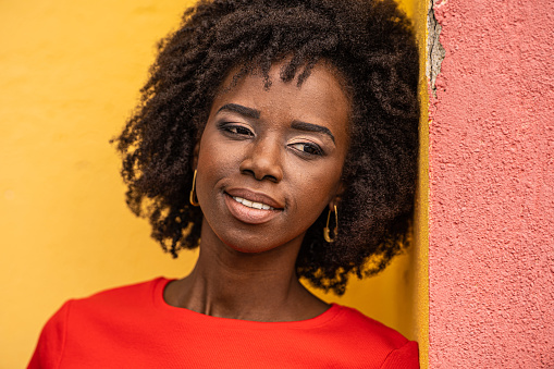 Аttractive african young woman, wearing red t-shirt, posing in front of a yellow background