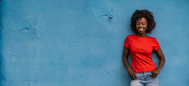 Аttractive african young woman, wearing red t-shirt, posing in front of blue background