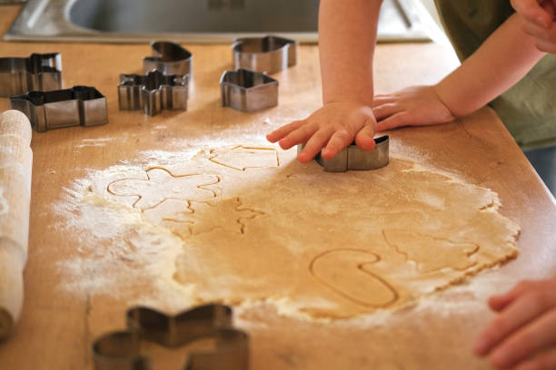 children rolling out cookie dough with a wooden rolling pin on the kitchen countertop. metal baking molds. joy of childhood baking, family traditions, homemade treats. siblings helping to mom together - pastry cutter family holiday child 뉴스 사진 이미지