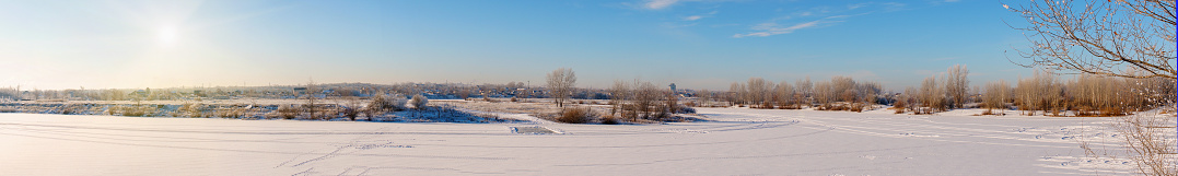 Winter landscape panorama. A winter river and a village in the distance covered with snow