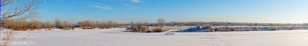 Winter landscape panorama. A winter river and a village in the distance covered with snow