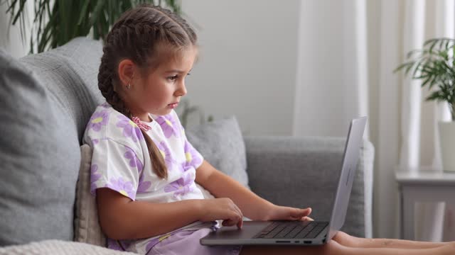 Side view of happy and smart little girl using laptop at home. Five year old girl try to use smart devise