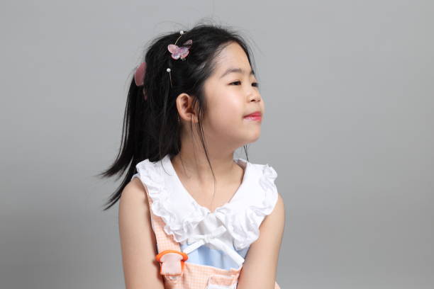 The little cut Asian girl with fancy dressed standing on the grey background.