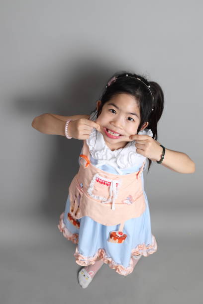 The little cut Asian girl with fancy dressed standing on the grey background.