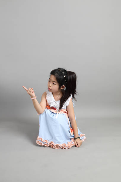 The little cut Asian girl with fancy dressed sitting on the floor in grey background.