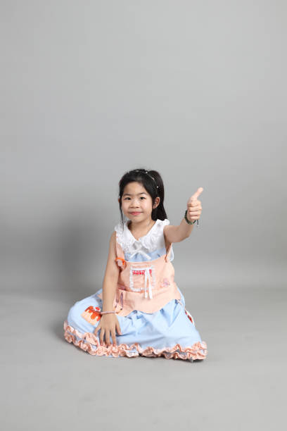 The little cut Asian girl with fancy dressed sitting on the floor in grey background.