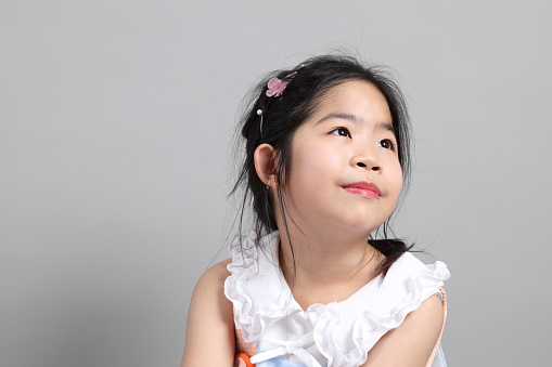 The little cut Asian girl with fancy dressed standing on the grey background.