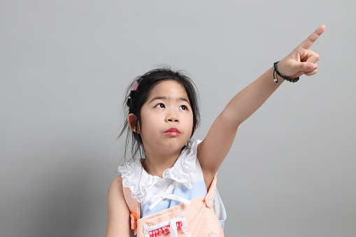 The little cut Asian girl with fancy dressed standing on the grey background.