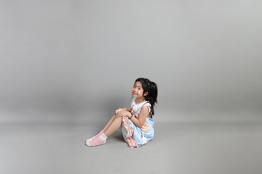 The little cut Asian girl with fancy dressed sitting on the floor in grey background.