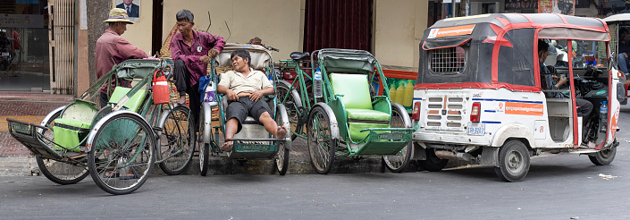 Phnomh Penh, Cambodia on Feb 24, 2024: Tuk Tuk and Rikshaw drivers having a chat and waiting for business picking up after lunch time